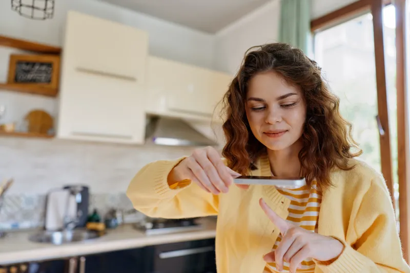 Cheerful woman in a cozy kitchen, focused on cutting a small item, warm natural light, casual outfit, neat counter, home atmosphere, everyday cooking moment indoors