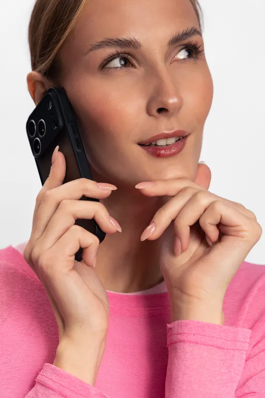 Young woman in pink sweater talks on smartphone, thoughtful expression on face. Modern communication concept with close-up portrait and soft lighting on white background.