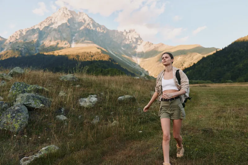 Young woman hiking in mountain landscape wearing shorts and backpack. Sunny day with clear sky, concept of outdoor lifestyle and adventure travel.