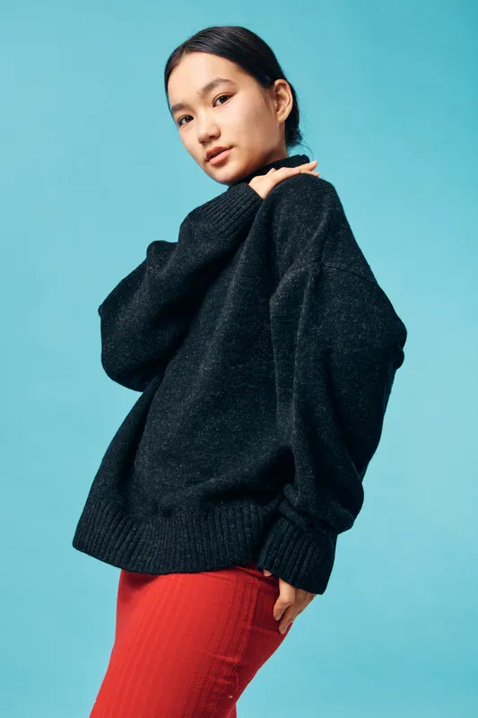 Young woman in black oversized sweater and red pants posing against blue background for fashion, style and casual outfit in studio. Portrait, trendy, confident and model with natural makeup.