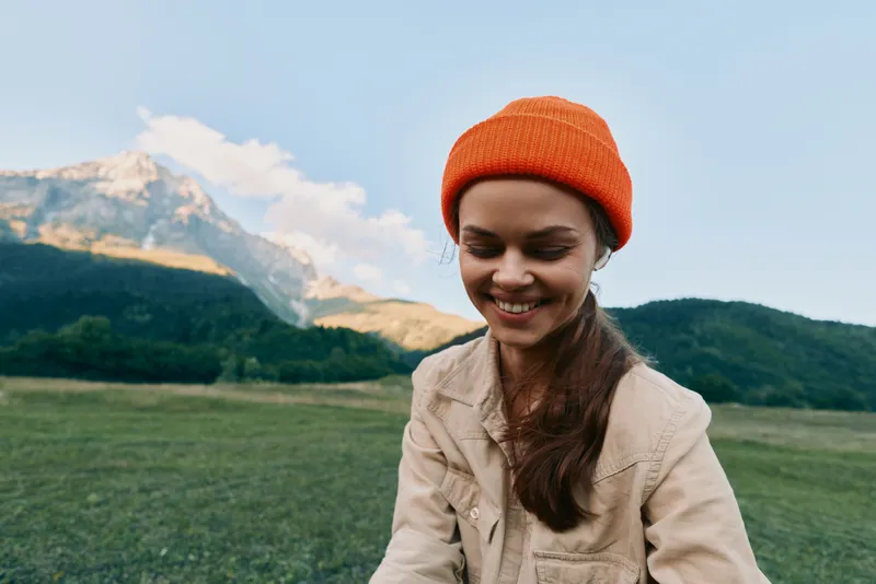 Cheerful woman outdoors, smiling in a natural landscape, casual pose, sunlit countryside, soft breeze, vibrant colors, mountains in distance, relaxed mood, with bright skies