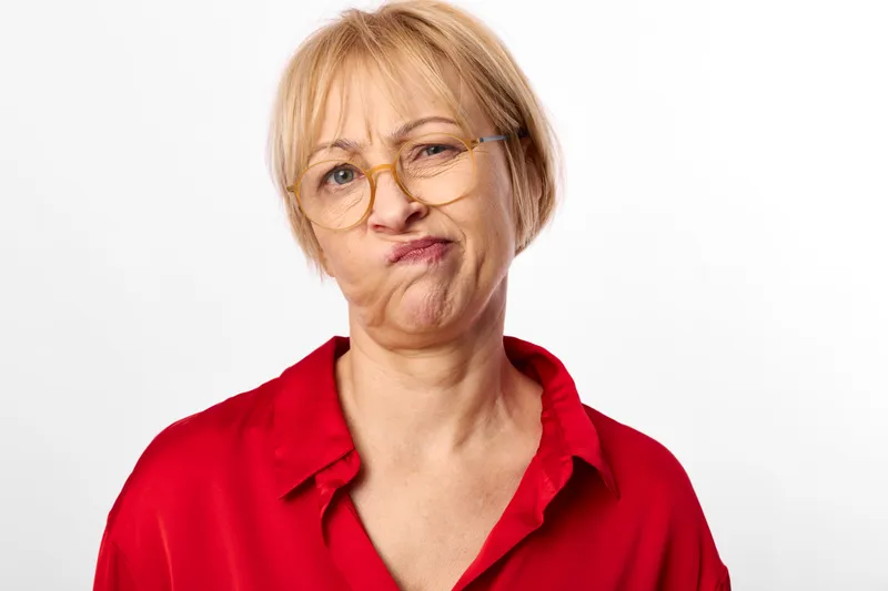 Stressed senior woman with glasses, red polo shirt, worry and sadness on a white studio background, tight face expression, concept of anxiety, mental stress