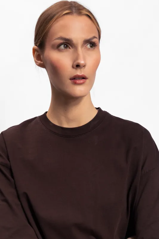 Young woman with blond hair wearing dark brown sweater looks to the side with serious expression on white background. Concept of contemplation, fashion, and casual style portrait.