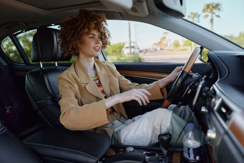 Young woman drives a car with a relaxed smile, retro film colors tinting the interior, sunlit road ahead as she concentrates on the drive and enjoys the moment.