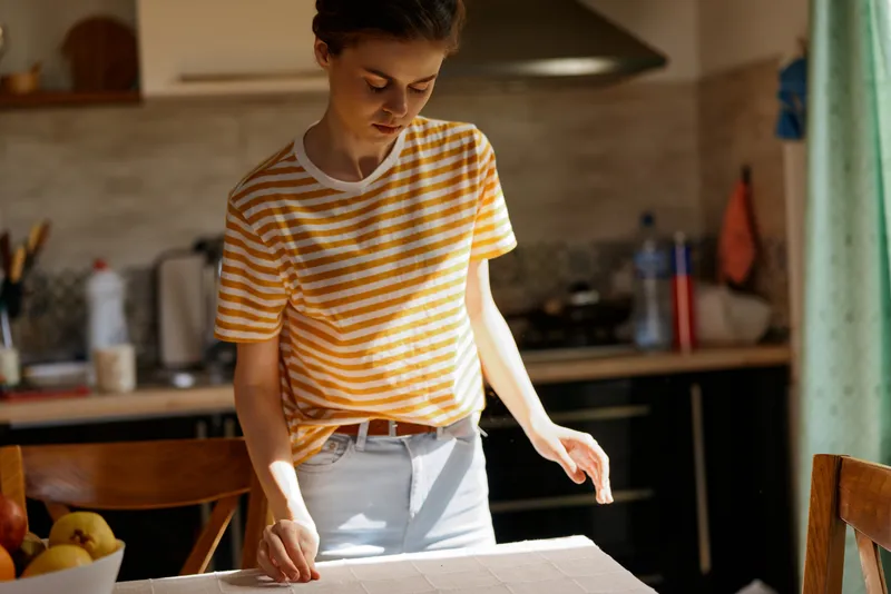 Woman in a bright home kitchen, rolling dough on a flour dusted counter, casual striped shirt, soft sunlight, focused expression, warm cozy mood, everyday cooking moment