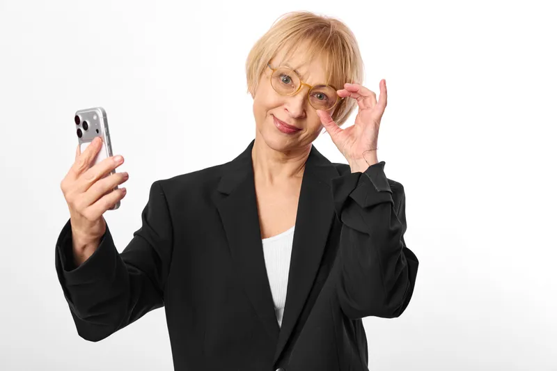 Senior businesswoman, woman holding smartphone and touching glasses, portrait on white background, focused expression, communication and technology concept, stress
