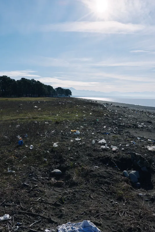 Deserted beach littered with trash and plastic debris along a rocky shoreline under a bright sky, highlighting environmental pollution and the need for cleanup.