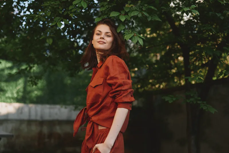Woman lifestyle outdoor portrait fashion red natural sunlight smiling confident in a park setting, relaxed posture and warm mood, conveying everyday wellness and self expression