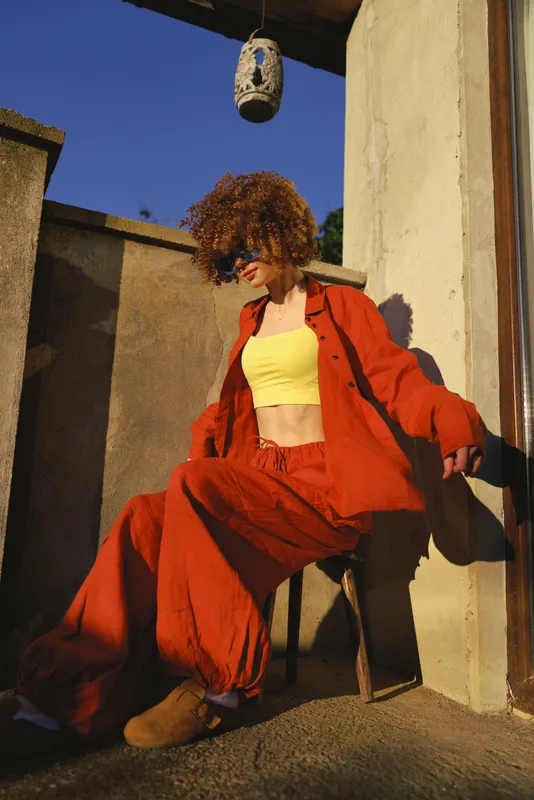 Woman lifestyle shoot on a sunny outdoor terrace, fashion forward red suit and yellow top, relaxed pose, candid moment showcasing bold color blocking and confident attitude