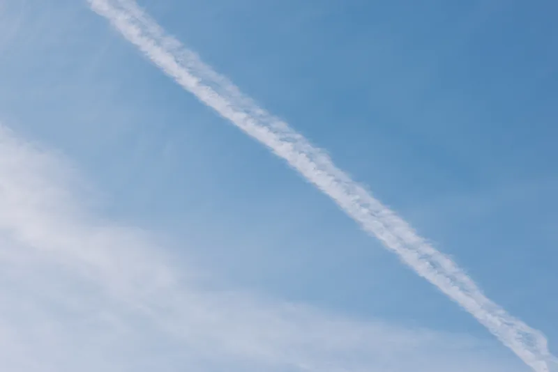 Blue sky with a diagonal contrail slicing across, with wispy clouds on the edge, creating a calm aviation moment ideal for travel, nature, weather, and serene outdoor inspiration.