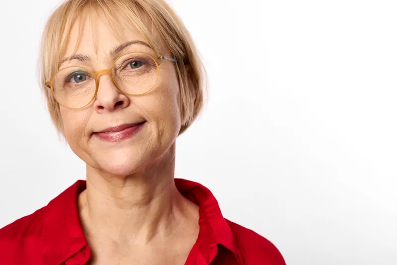 Woman senior glasses smiling portrait health vision care studio white background, elderly model, soft light conveys wellbeing calm today and confidence