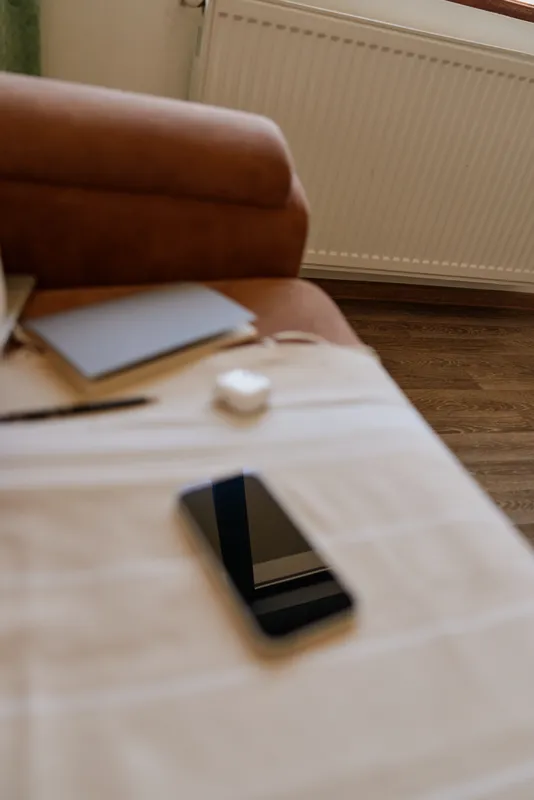 Home lifestyle scene with a sofa, coffee table, scattered papers, and a smartphone resting on the surface, warm natural light creating a calm, casual working or relaxing mood