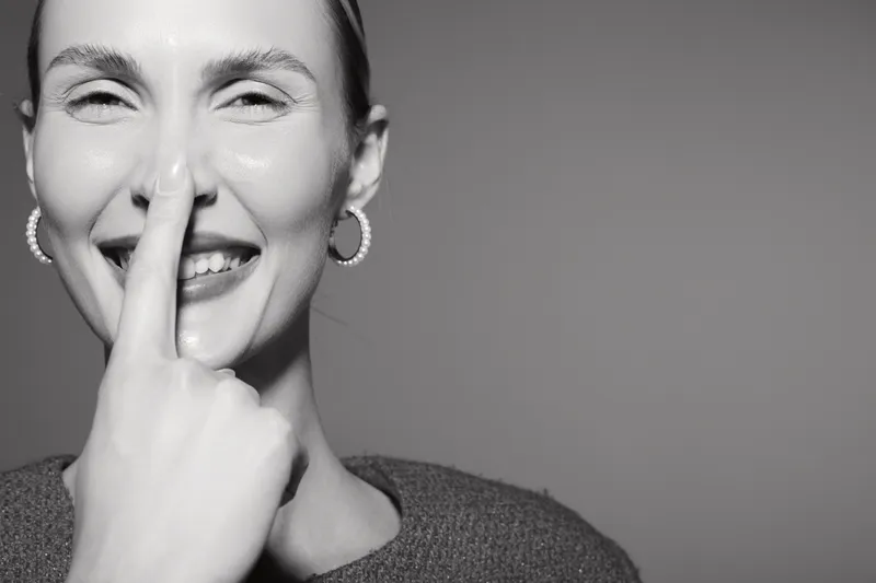 Happy white woman with light skin smiling and holding finger on nose in monochrome close-up portrait.