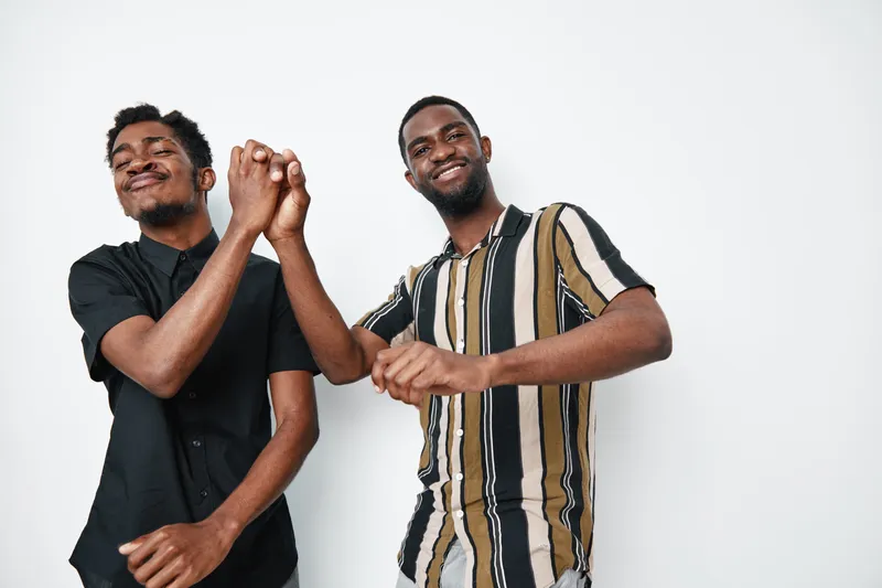 Two young black men with dark skin smiling and dancing together in casual clothes on white background. Friends enjoying music and having fun in studio with happiness.