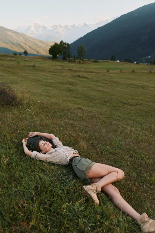 Relaxed woman lies on a grassy meadow in a wide field, enjoying outdoor lifestyle under warm sun, casual pose and peaceful nature vibes in a rural landscape