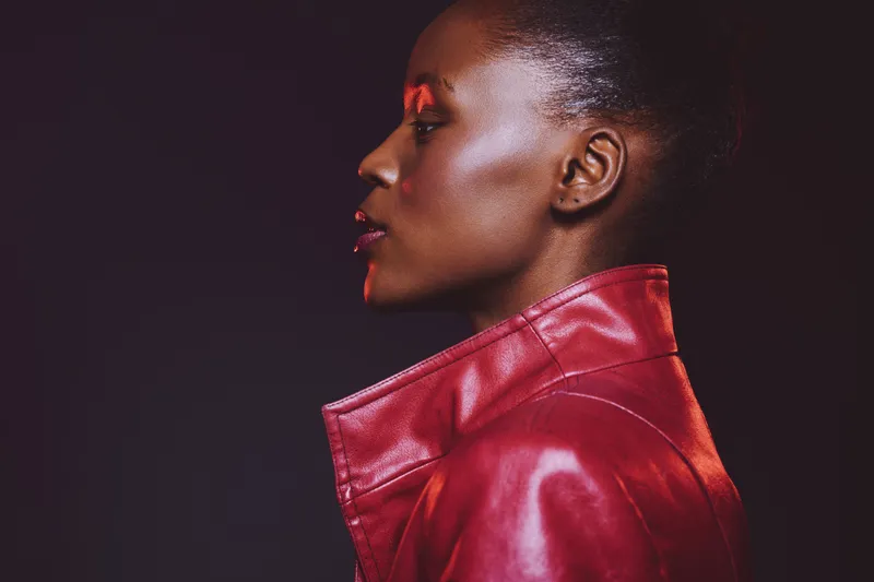 Profile of a dark skinned African woman wearing a red leather jacket against a black background. The image conveys fashion, elegance, and modern style with dramatic lighting.