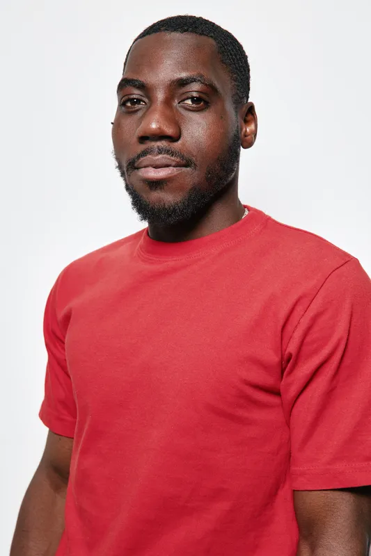 Portrait of confident black man with dark skin wearing red t shirt looking at camera isolated on white background. African ethnicity, casual style and natural expression in studio lighting.