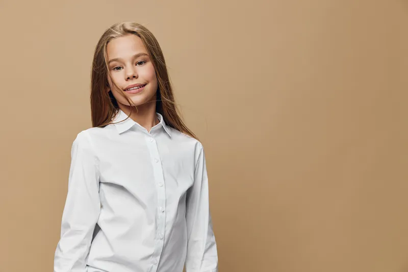 Girl child wearing white shirt standing smiling with long hair against beige background looking confident happy and casual studio portrait with natural expression.