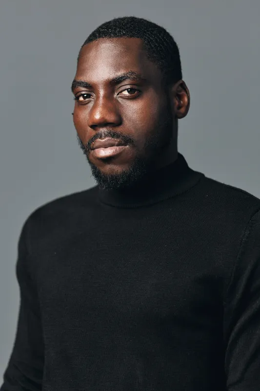 African man portrait with beard wearing black turtleneck sweater in creative conceptual visual style studio. Serious expression, dark skin, closeup with soft lighting on gray background.