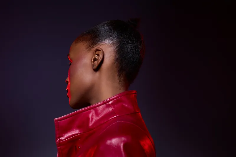 Profile of a black African woman with dark skin wearing a red leather jacket against a dark background. Concept of fashion, style, and modern portrait with dramatic lighting and color contrast.