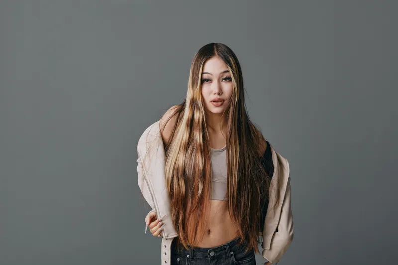 Young woman with long hair posing in casual clothes against gray background, wearing crop top and jacket for fashion portrait and style concept.
