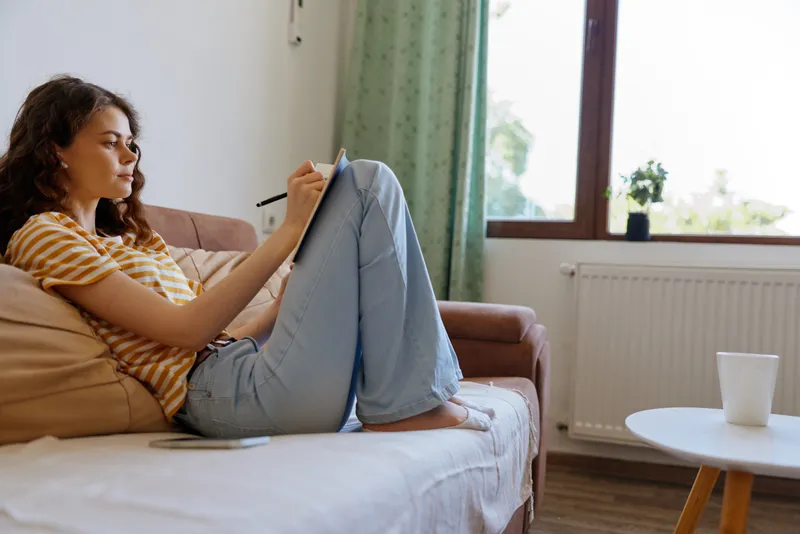 Casual woman at home, sitting on a sofa with a tablet, relaxed posture, soft afternoon light, focused expression, cozy living room, lifestyle in a private space