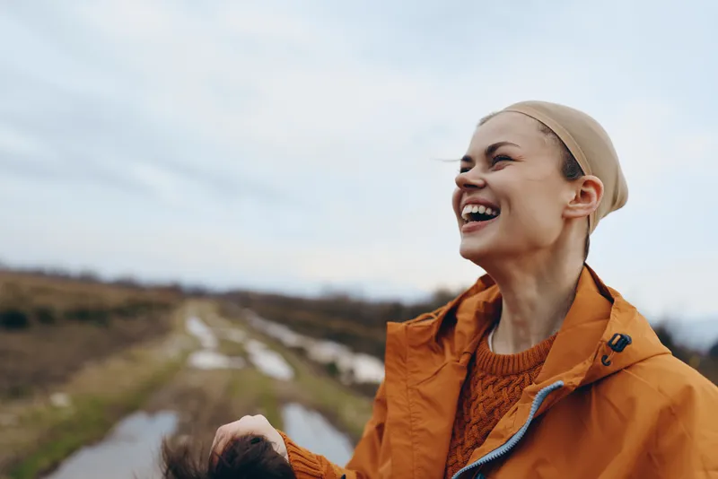 Woman hiking outdoors in orange jacket, smiling and laughing, enjoying fresh air in nature landscape, lifestyle travel, hills trail and cloudy sky, motion blur daylight