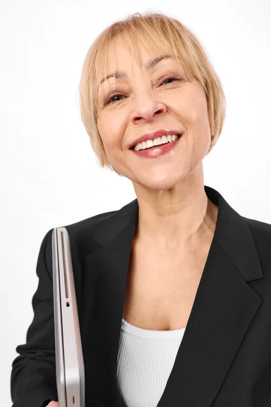 Woman senior blonde business portrait, with confident smile, wearing suit, holding clipboard with documents, studio white background, warm professional mood.