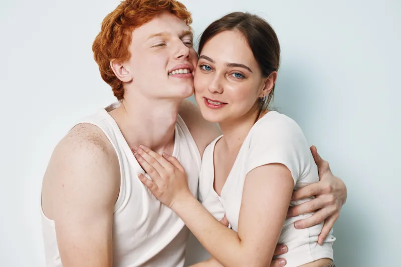 Couple, man and woman in white shirts embracing and smiling in studio. Young people with happy expression and close body contact on light background for love and relationship.