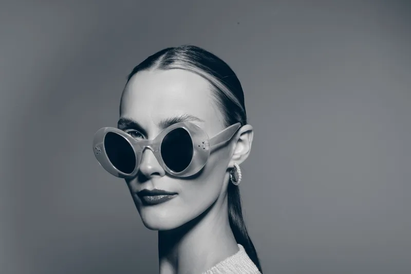 Portrait of a fair skinned Caucasian woman wearing large round sunglasses and hoop earrings in a studio. Concept of fashion, style, glamour, and confident female model.
