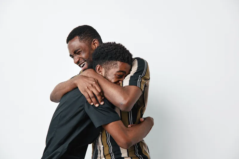 Two black men with dark skin hugging and smiling in casual clothes on white background. African ethnicity, friendship and happiness with emotional connection and joy.