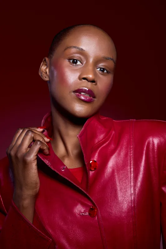 Portrait of elegant dark skinned African woman wearing shiny red leather jacket on red background. Fashion concept with confident model and glossy makeup in studio lighting.