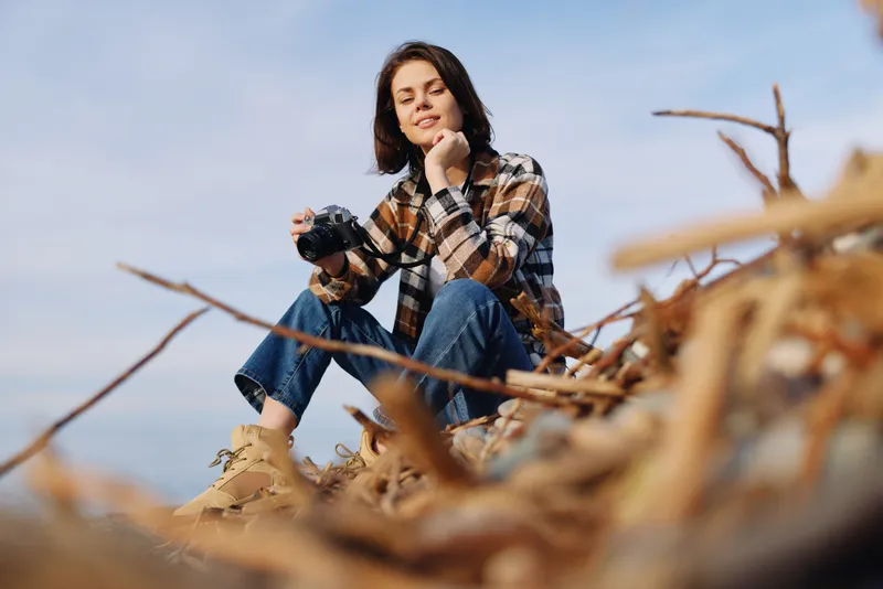 Woman outdoor casual portrait sitting on sandy dunes, plaid shirt and jeans, relaxed mood, natural light, breeze in hair, beach landscape and clear sky, serene lifestyle moment captured on location