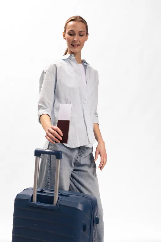 Young woman with suitcase holding passport and boarding pass in hand, ready for travel. Casual outfit, isolated on white background. Concept of tourism, vacation, and journey.