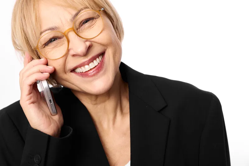 Business woman smiling while talking on phone, wearing eyeglasses, senior adult close up portrait, office style professional communication, friendly demeanor