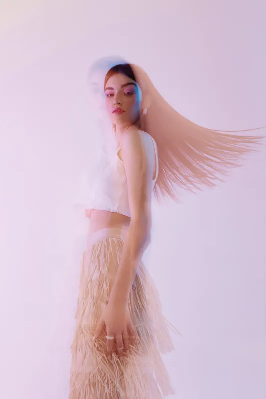 Young woman beauty fashion model with long hair in motion wearing a stylish fringed skirt and white top on a light background. Concept of elegance and modern style.
