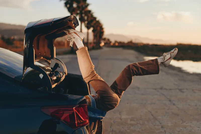 Woman driving a convertible car on the road at sunset, hands on steering wheel, casual jacket and sunglasses, warm cinematic light, outdoor travel lifestyle near ocean