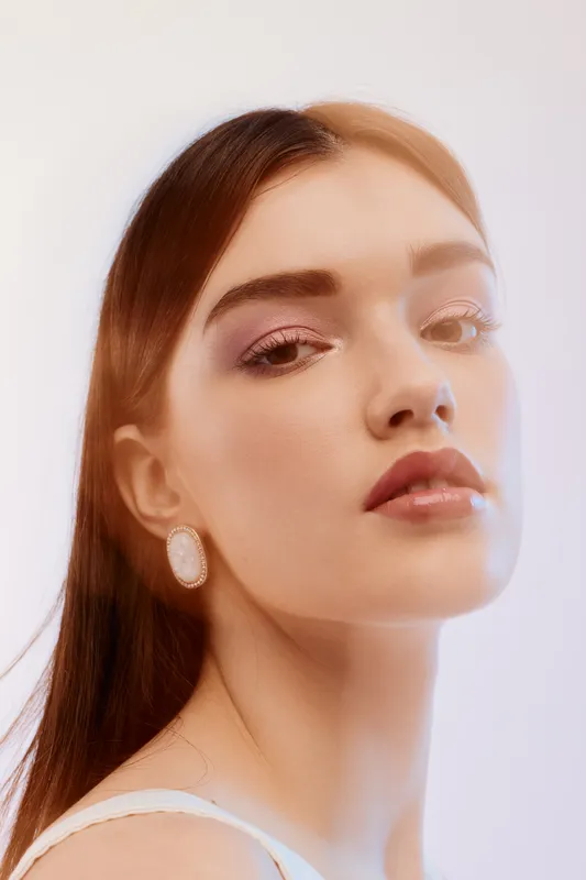 Close-up portrait of a young woman with red hair and natural makeup looking confidently at the camera. Soft lighting highlights her beauty, fashion, and elegance concept.