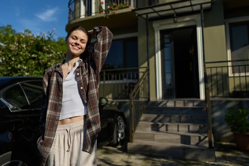 Portrait of a smiling woman enjoying a casual outdoor lifestyle, wearing a plaid shirt and light clothes, standing on a sunny neighborhood residential street with a cheerful mood