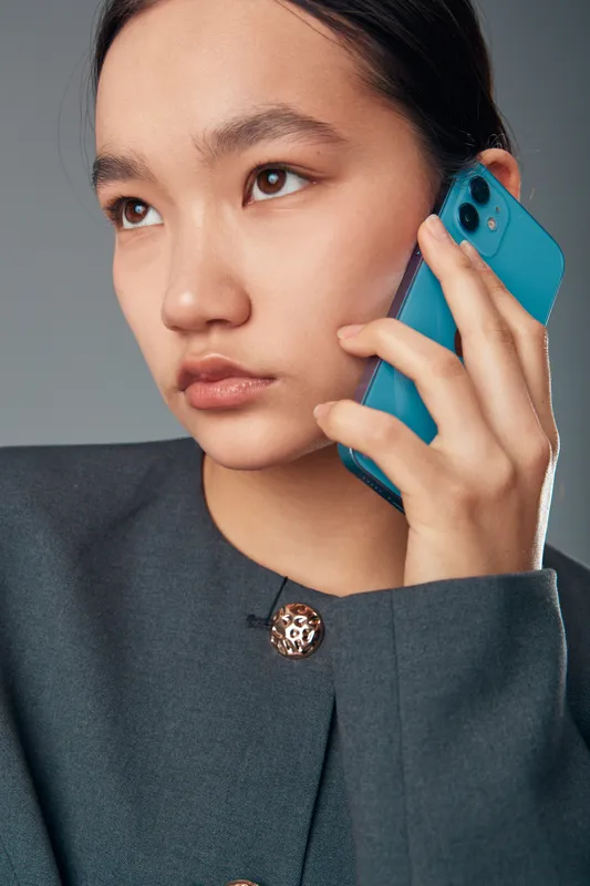 Young woman with serious expression holding smartphone to ear for communication and business conversation. Closeup portrait with modern device and focused gaze on face.