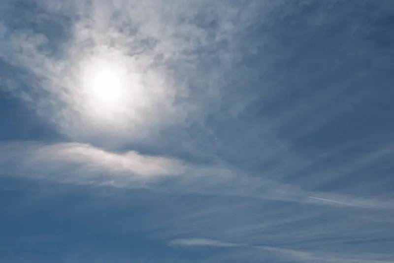 Blue sky with a bright sun and wispy clouds, clear horizon, and radiant daylight creating a calm, open atmosphere suitable for outdoor scenes and positive mood.