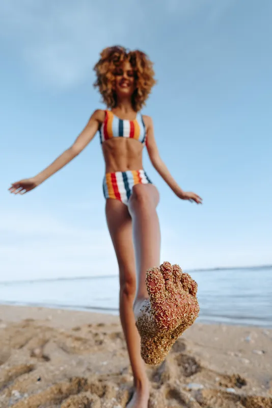 Beach summer scene, curly haired girl running on sandy beach, splashing sea water, holding small starfish in her hand, colorful swimsuit, sunny day, open sky background relaxed, today