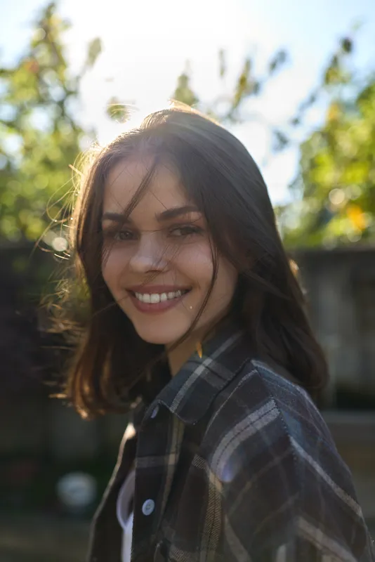 Woman lifestyle outdoor portrait of a smiling woman in a plaid shirt, sunlit garden setting, casual vibe, natural expression, candid moment in daylight and warmth