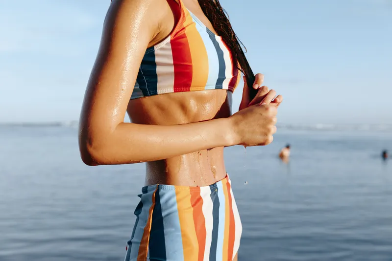 Woman, beach, ocean, striped, dress, summer, vacation, arms, crossed, sunlight, calm outdoor portrait of a woman by the sea, arms crossed relaxed posture, bright warm light, seaside lifestyle travel