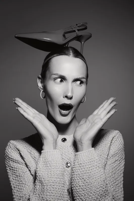 Surprised white caucasian woman with light skin holding hands near face and high heel shoe on head. Fashion and expression concept.