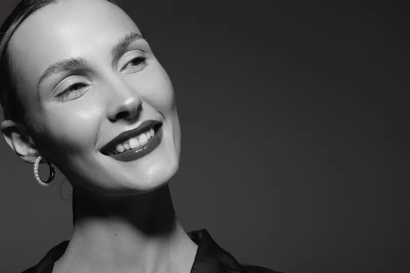 Smiling white woman with fair skin and earrings looks away in black and white studio portrait. Concept of happiness, elegance, and beauty.