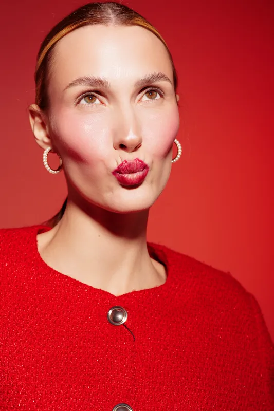 Young woman with red lipstick and earrings makes a kiss face on red background. Fashion portrait with bright makeup and stylish red outfit. Concept of beauty and glamour.