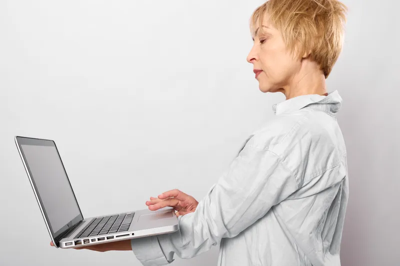 Woman typing on laptop in profile indoors, casual studio setting, calm smile, focused computer work, keyboard and screen visible, technology and internet