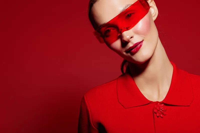 Portrait of a stylish woman wearing red sunglasses and a red textured jacket against a red background. Fashion concept with bold colors and modern accessories.