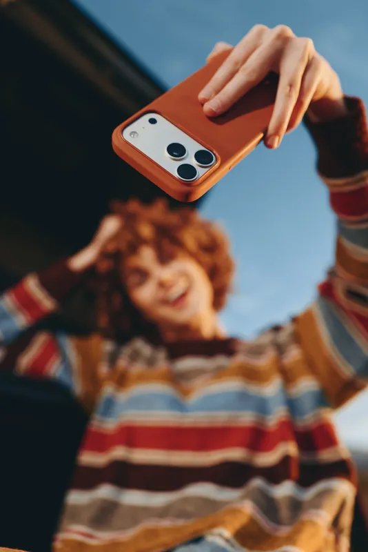 Woman holding smartphone, hand filming a child selfie, curly hair, striped sweater, outdoor lifestyle, soft daylight, warm smile, shallow focus, playful striped colors, relaxed family moment